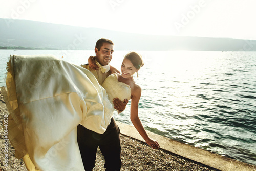 Happy handsome groom holding bride in his arms on beach at sunse © IVASHstudio
