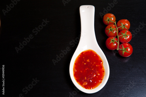 spicy tomato sauce in a gravy boat near cherry tomatoes on a dar