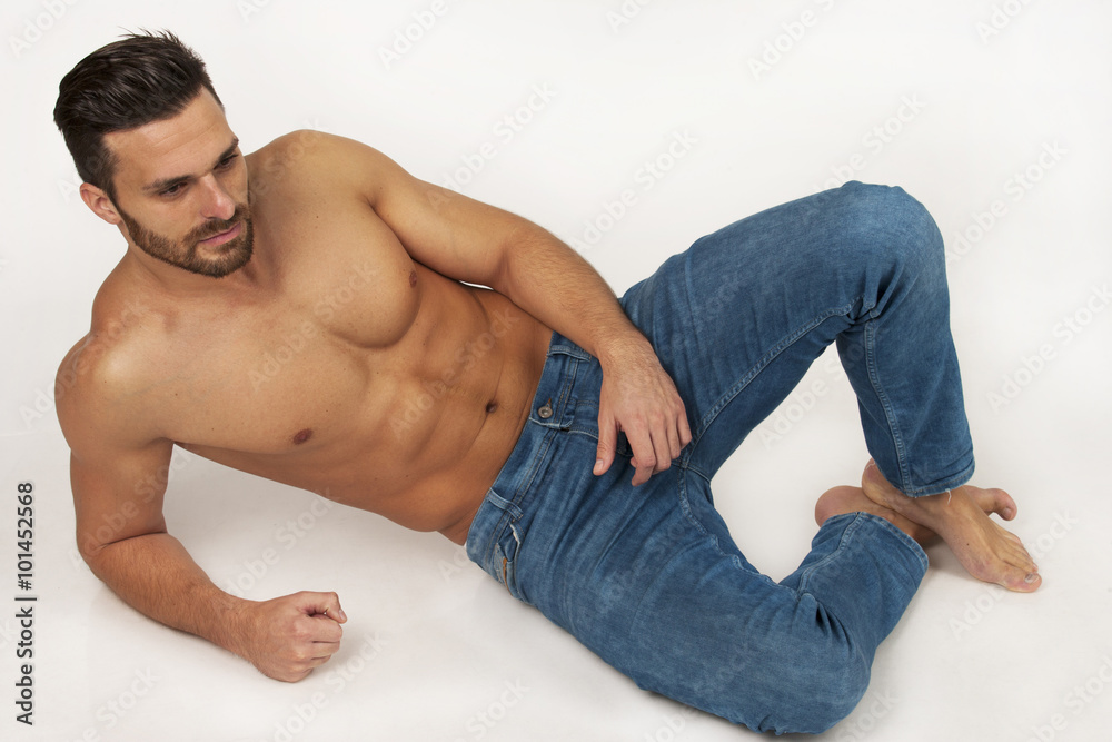 Handsome modern strong muscular man in blue jeans laying on white Handsome modern strong muscular man in blue jeans laying on white