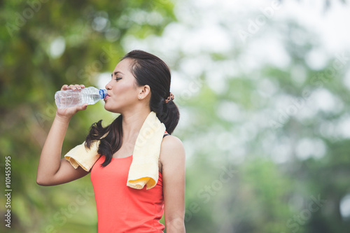 Young asian woman drinking water after doing excercise outdoor i