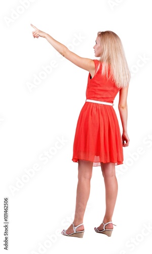 Back view of young blonde woman pointing at wall.