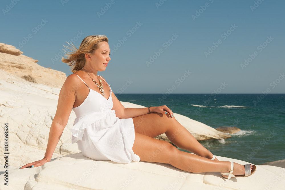 Young woman in summer dress sitting on the rocks by the sea Young woman in summer dress sitting on the rocks by the sea