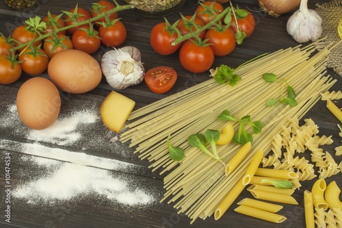 Spilled flour. Pasta and vegetables on a wooden table. Dietary food. Pasta, tomatoes, onion, olive oil and basil on wooden background.
 photo