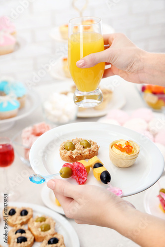 Woman holding glass of juice and plate with snacks on buffet background