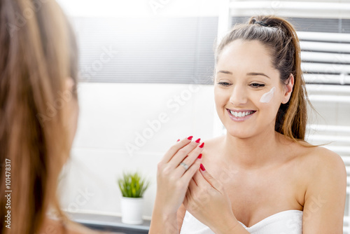 Attractive girl putting anti-aging cream on her face