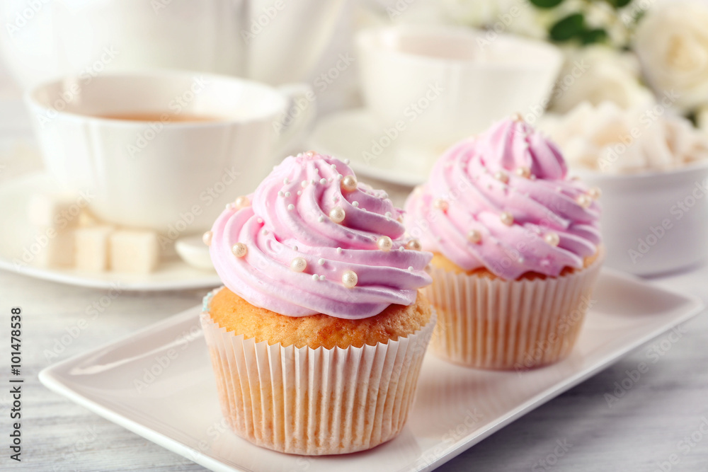 Two tasty pink cupcakes with cups of tea on light background