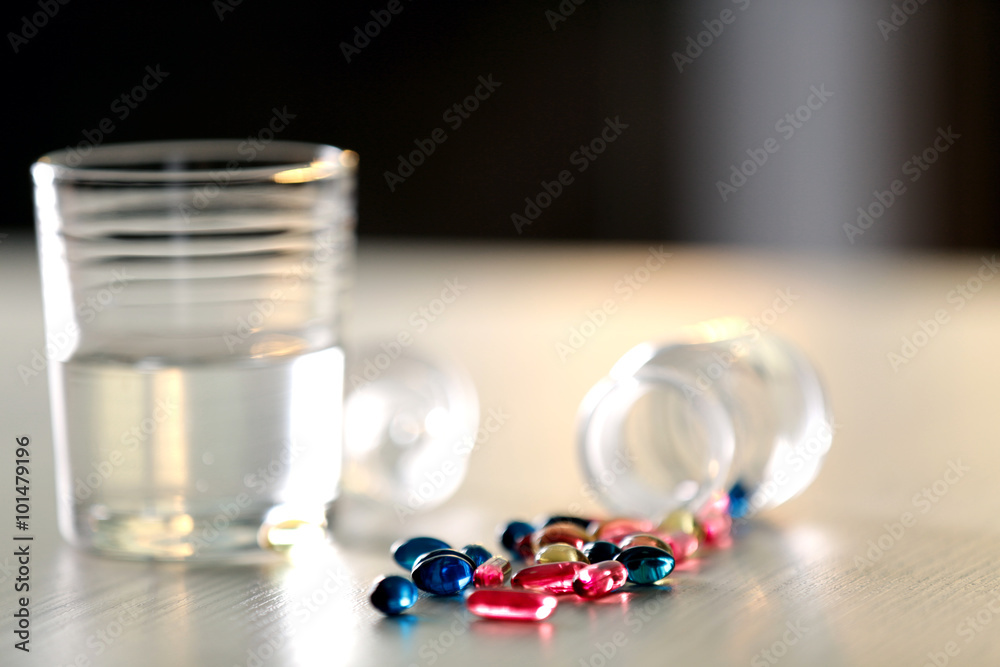 Φωτογραφία Pile of blue and red capsules with glass of water on the table, close up