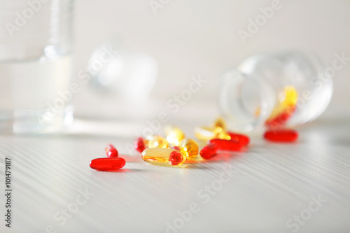 Colourful capsules spilled from pill bottle and glass of water on the table, close up