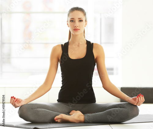 Health concept. Young attractive woman does yoga exercise in the gym against window