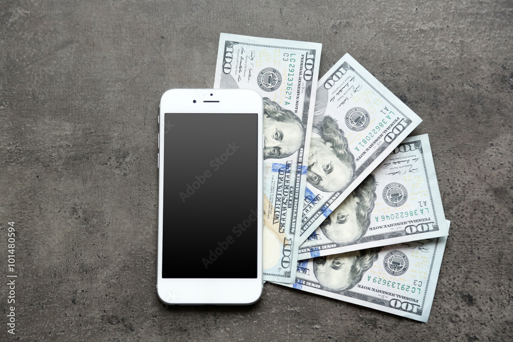 Fotografie Smart phone with dollar banknotes on grey background