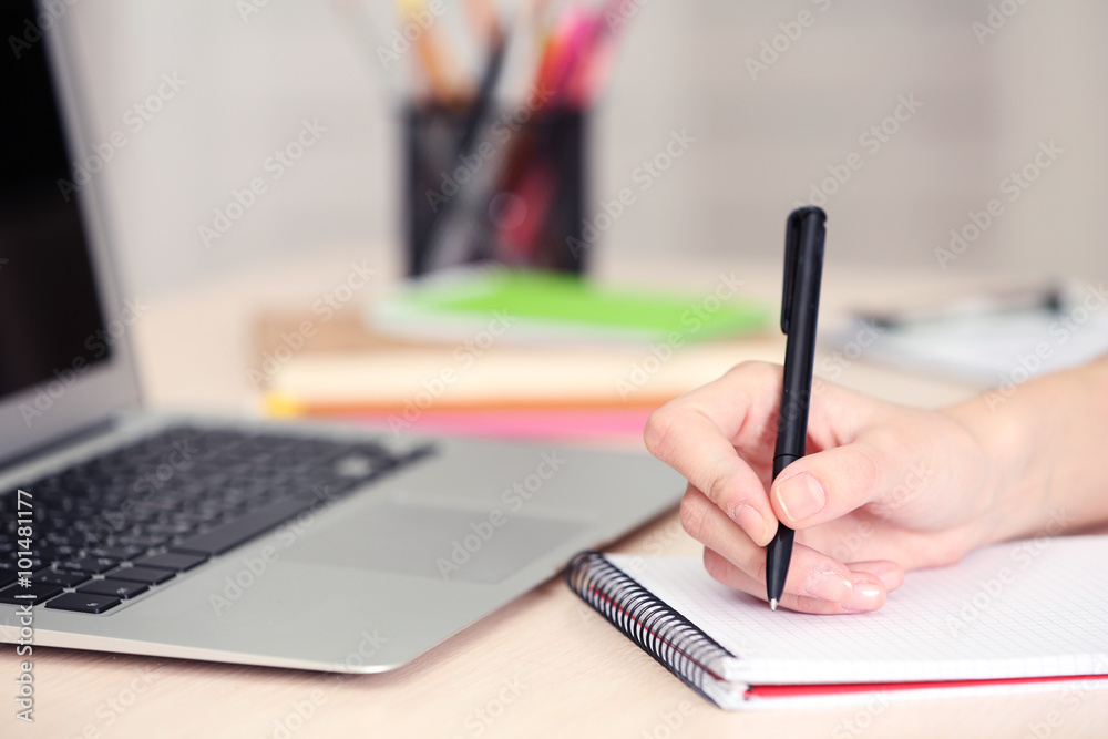 Woman making notes with a laptop beside Woman making notes with a laptop beside