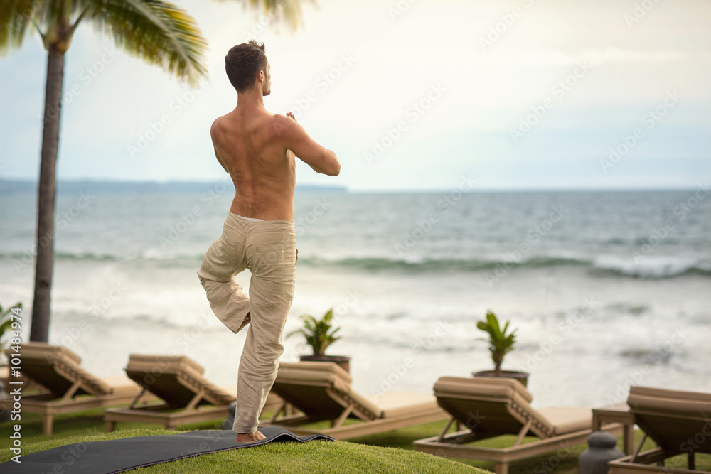 Fotografie young man making yoga exercises on beach from back