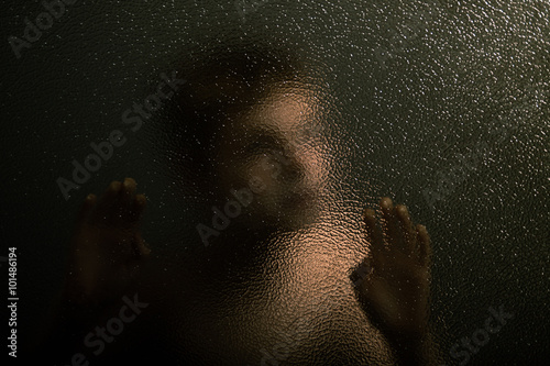 Scary Young Boy Leaning Against a Textured Glass
