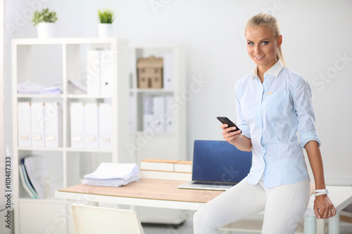 Young business woman standing in office talking on her mobile phone
