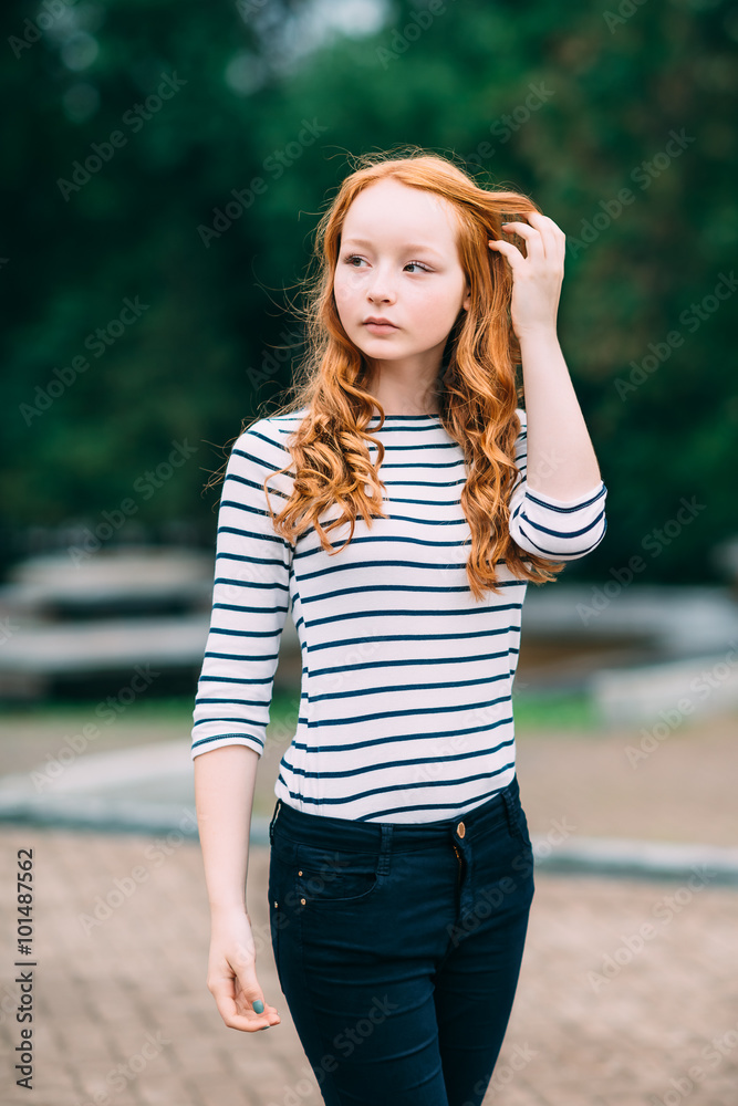 Outdoor portrait of beautiful girl with long curly red hair and green eyes.  Young redhead woman touching her ginger hair. Teenage red-haired girl  standing in summer park. Femininity concept Stock Photo |