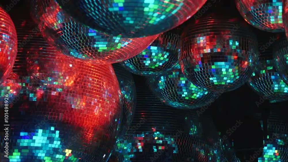 Mirror balls reflect rays of colored lights. Colorful reflective disco mirror ball with glinting highlights spinning slowly on a blurry colored background in disco club. The light show at night.