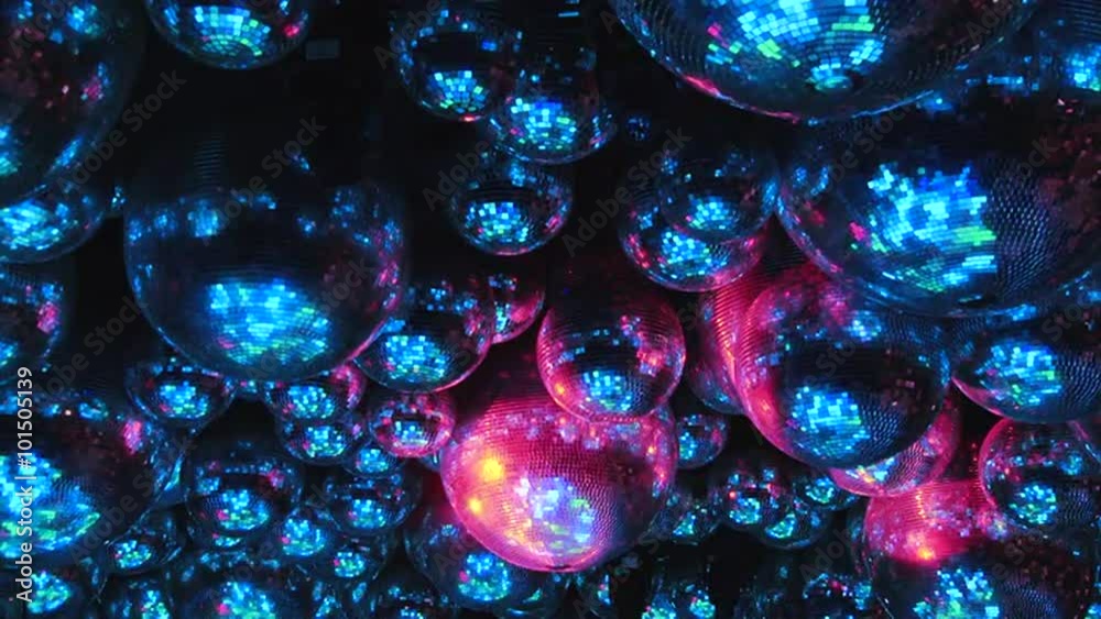 Mirror balls reflect rays of colored lights. Colorful reflective disco mirror ball with glinting highlights spinning slowly on a blurry colored background in disco club. The light show at night.