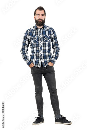 Confident serious hipster in plaid tartan blue shirt with hands in pockets. Full body length portrait isolated over white studio background.