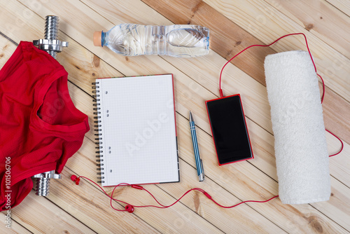 Sport Equipment. Barbell, Red Shirt, Bottle Of Water, Towel, Smart Phone With Earphones And Notebook To Workout Plan On Wooden Boards. Sport Fitness Background