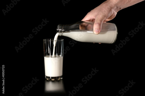 man pours cow's milk from glass bottles in a glass