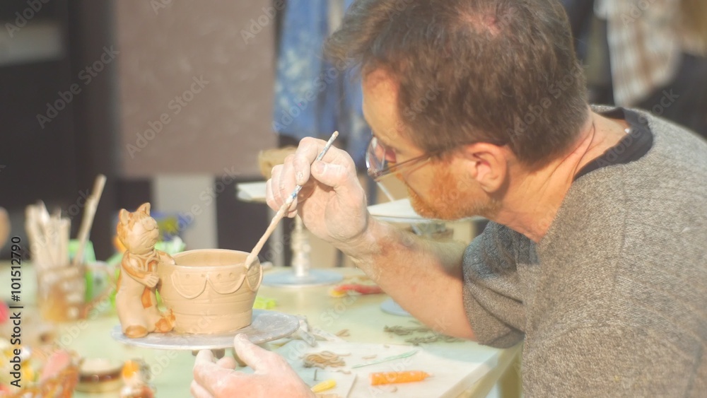 Man is Painting a Clay Pot With Cat Figurine Glazing Pot by Brush Painting Attentively at the Table Kids Little Girls are Sitting People Silhouettes Man is Painting a Clay Pot With Cat Figurine Glazing Pot by Brush Painting Attentively at the Table Kids Little Girls are Sitting People Silhouettes