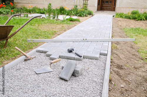 Photo Bricklayer places concrete paving stone blocks for building up a patio, using ha