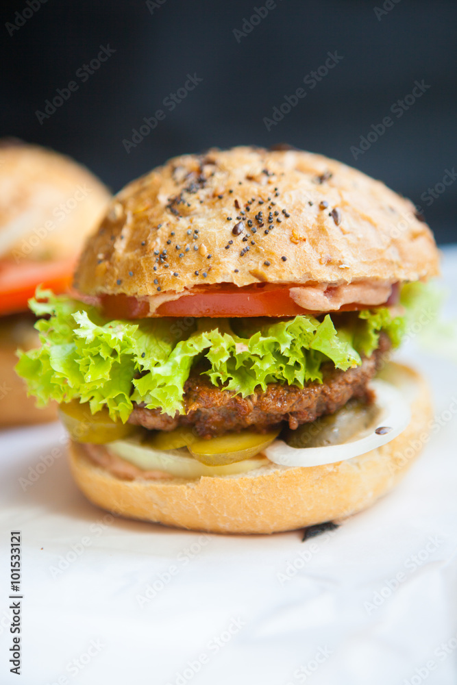 Fresh homemade burgers on wooden cutting board over dark background Fresh homemade burgers on wooden cutting board over dark background