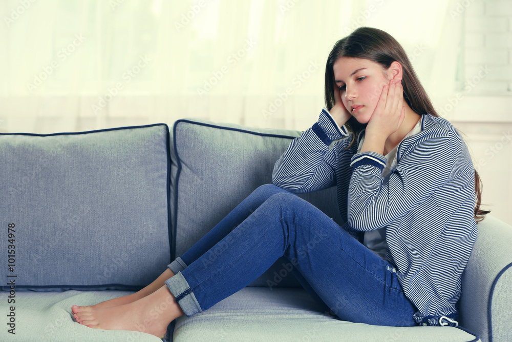 Young upset girl sitting on the sofa in her room Young upset girl sitting on the sofa in her room