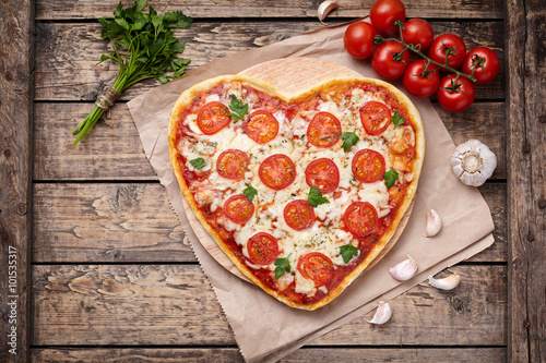 Heart shaped pizza margherita vegetarian love concept with mozzarella, tomatoes, parsley and garlic on vintage wooden table background