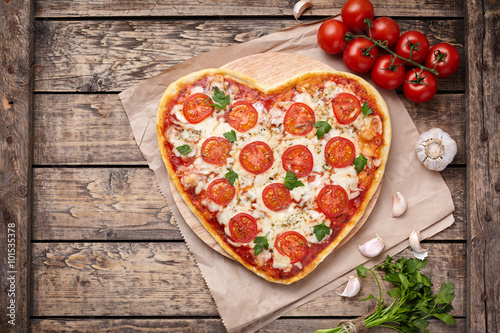 Heart shaped pizza margherita vegetarian love concept with mozzarella, tomatoes, parsley and garlic composition on vintage wooden table background. 