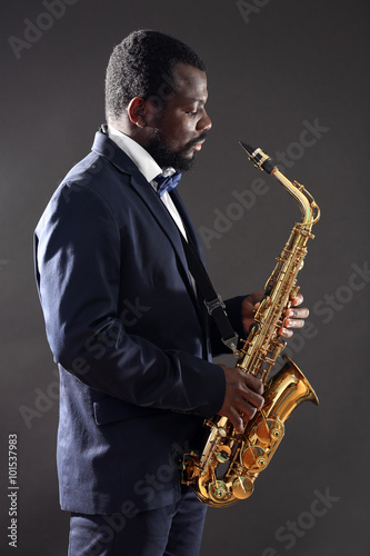 African American jazz musician playing the saxophone on grey background