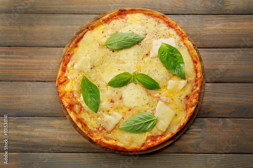 Tasty pizza decorated with basil  on wooden background, close up