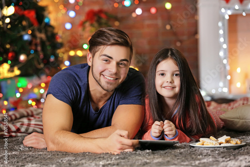 Older brother and little sister with tablet sitting and eating cookies in Christmas living room