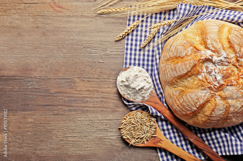 Fresh baked bread, flour, wheat in spoons and napkin on the wooden background