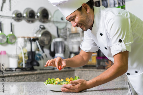 Smiling asian chef put small tomato in vegetarian salad on kitchen background.