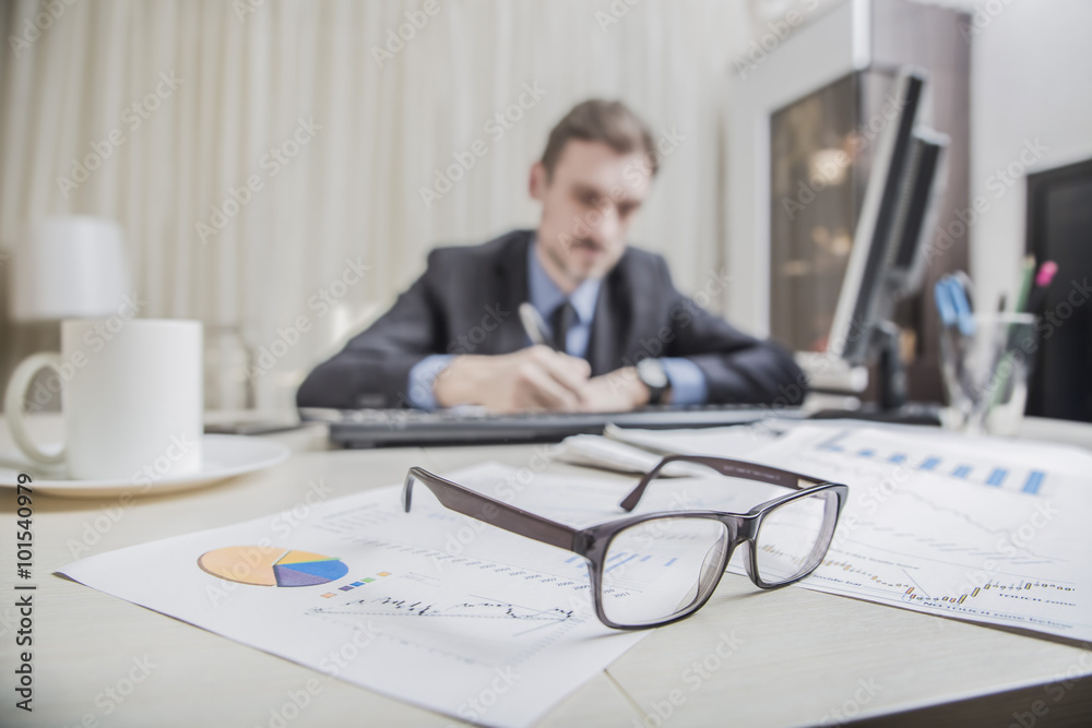financial chart near dollars seen by unfocused glasses (only blurred out of focus silhouette of a businessman working at the Desk in the office visible viewed ) financial chart near dollars seen by unfocused glasses (only blurred out of focus silhouette of a businessman working at the Desk in the office visible viewed )