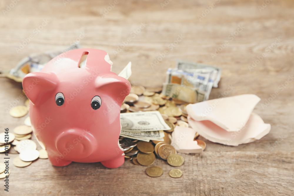 Fotografie Broken piggy bank with cash and coins on wooden background
