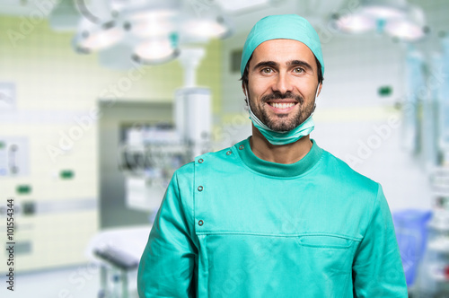 Smiling surgeon crossing his arms while standing in a surgical room photo