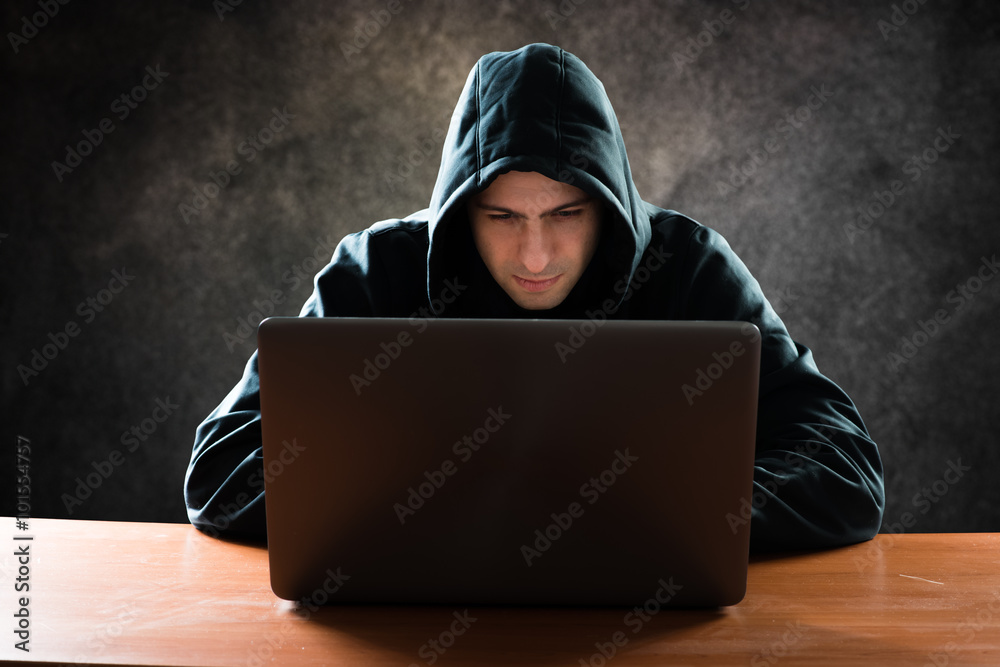 Hooded computer hacker stealing information with laptop Hooded computer hacker stealing information with laptop