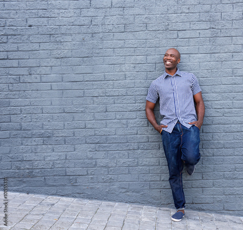 Smiling african guy leaning against gray wall