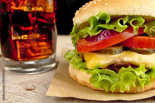 Big cheeseburger with glass of cola on wooden table