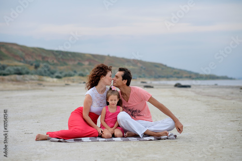Happy family of three having fun sitting in the sand on beach