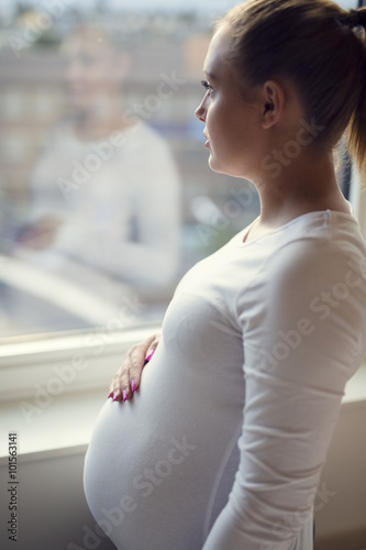 Young thoughtful pregnant woman looking out the window