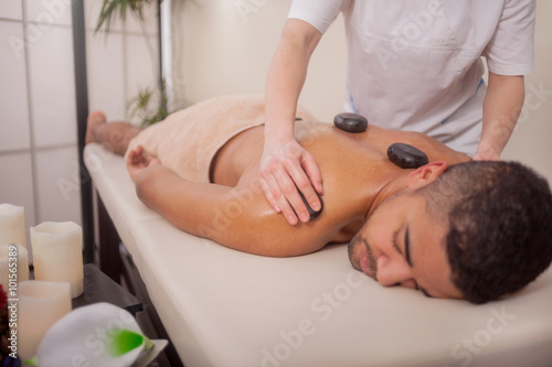 Masseur doing back massage with spa stones on man body in the sp