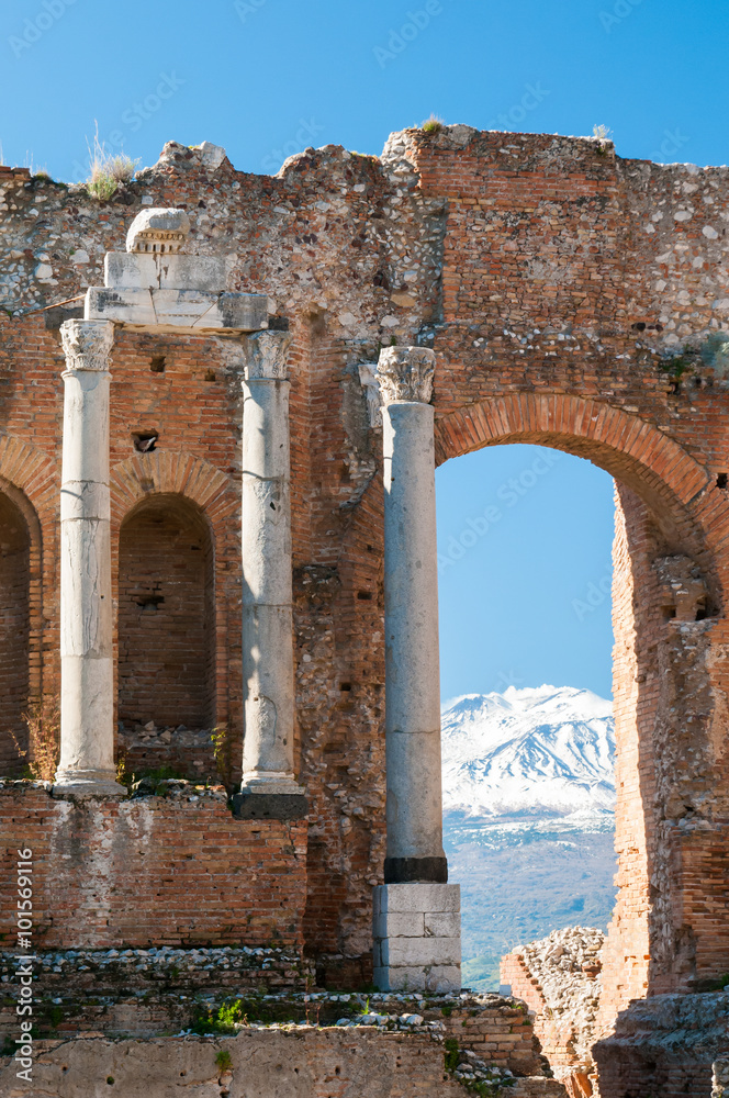 View of some columns in the stage of the greek theater in Taormina and a perspective of snowy mount Etna