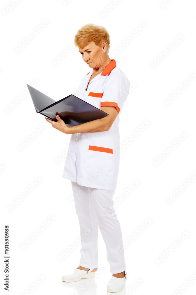 Elderly female doctor or nurse holds black binder and reads