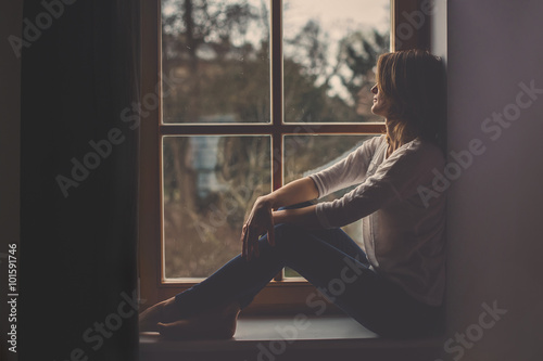 Young attractive woman, sitting on a window, looking outside © Tomsickova