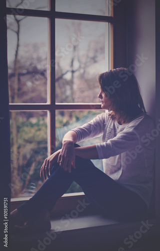 Young attractive woman, sitting on a window, looking outside