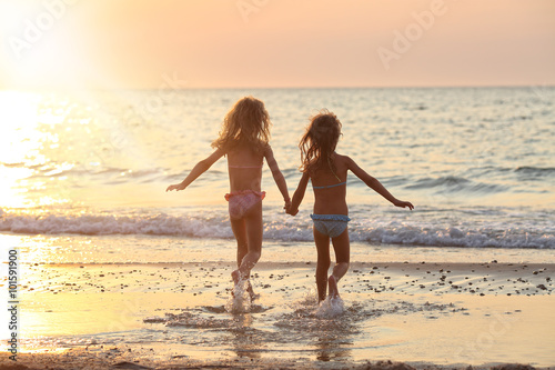 two sisters in beautiful swimsuits running holding hands by the sea photo