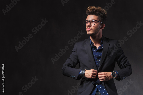 Fotografi skinny young man wearing glasses is fixing his jacket in studio